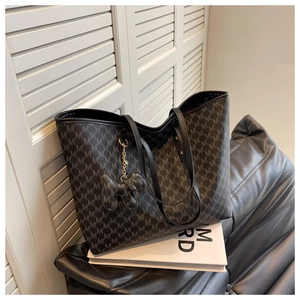 Close-up of a large grey tote bag with monogram pattern and elephant charm on books