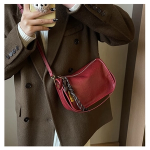 Détail d'un sac bandoulière en cuir rouge vin avec nœud tressé et pendentif métallique