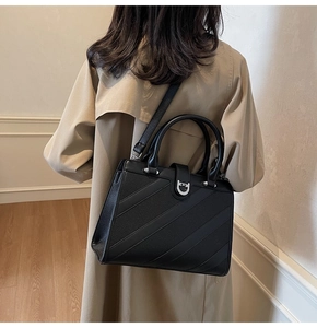 Dettaglio della borsa tote nera testurizzata con fibbia d'argento su un trench kaki