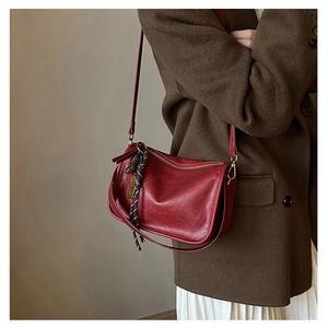 Sac bandoulière en cuir rouge brillant avec pendentif tissé sur un manteau