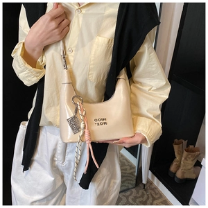 Gros plan du sac hobo en cuir verni crème avec logo en métal et pendentif tissé