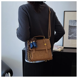 Detail of dark brown crocodile embossed backpack with a cute bear charm and tassel decoration
