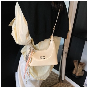 Détail du sac bandoulière crème verni avec logo métallique et pendentif déco
