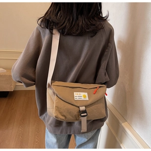 Detail der khakifarbenen Kuriertasche mit weißem Etikett und orangefarbenem Reißverschluss