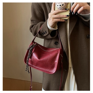 Détail d'un sac bandoulière rétro rouge foncé en cuir souple avec décoration tressée