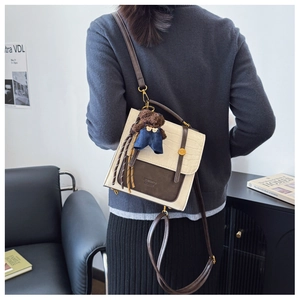 Rear view of model wearing a two-tone cream and brown crossbody bag with bear charm