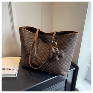 Detail of a large brown tote bag with M-letter print and a cute animal charm accessory