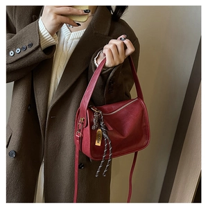 Détail d'un sac bandoulière rouge foncé avec breloque cacahuète et plaque dorée