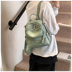 Close-up of mint green faux leather backpack with multiple zip pockets on a model
