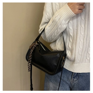 Détail d'un sac bandoulière en cuir noir avec foulard en soie et finitions dorées