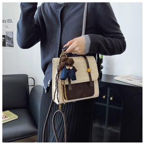 Detail view of cream crocodile-embossed leather tote with a brown plush bear charm