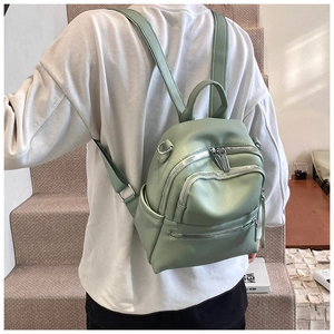 Detail of mint green backpack featuring litchi texture and silver zipper compartments