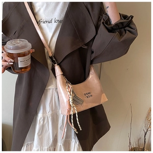 Détail du sac croissant rose métallisé avec gland tressé et logo doré sur trench-coat