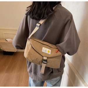 Detail einer khakifarbenen Messenger-Bag aus Nylon mit Schnallenverschluss und Smiley