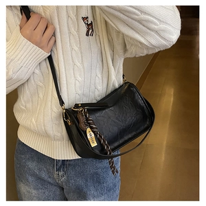 Détail du sac bandoulière noir en cuir texturé avec cordon marron et étiquette jaune
