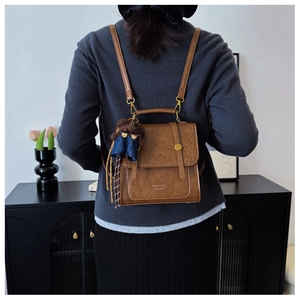 Detail of a brown leather backpack with crocodile pattern and a cute blue teddy bear charm