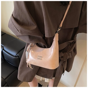 Gros plan d'un sac demi-lune en cuir verni rose avec logo argenté et détail de breloque
