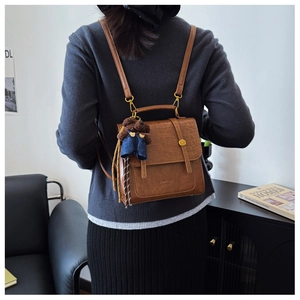 Detail of a brown crocodile pattern backpack with a cute teddy bear plush charm