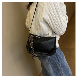 Détail du sac noir en cuir grainé avec breloque cacahuète et pompon sur pull blanc