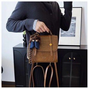 Detail of brown faux leather backpack featuring crocodile embossed texture and bear charm