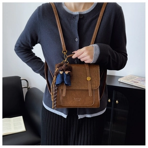 Detail view of brown crocodile texture backpack with cute bear pendant in a cozy setting
