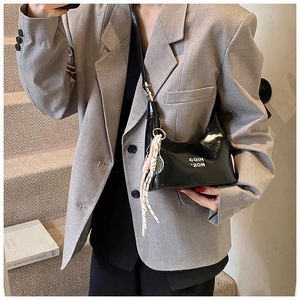 Détail du sac à bandoulière en cuir verni noir avec texte blanc et breloque en corde