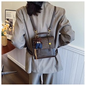 Close-up of brown crocodile texture backpack featuring a cute bear pendant and gold hardware
