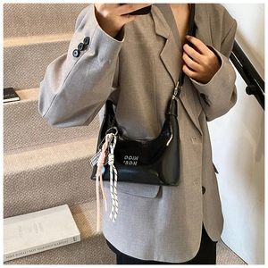 Détail du sac croissant en cuir verni noir avec corde tressée et breloque en métal