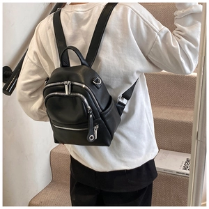 Detail view of a black faux leather backpack with multiple silver zippers on a model