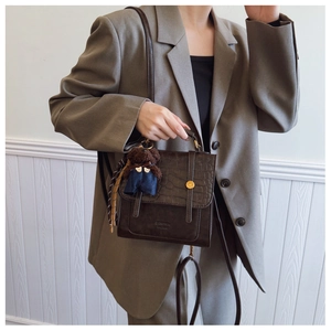 Detail of dark brown crocodile texture handbag with gold buckle and plush bear charm