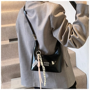 Détail du sac bandoulière en cuir verni noir avec logo argenté et breloque tressée