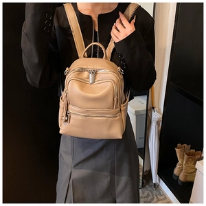 Detailed close-up showing light brown leather backpack texture and metal zipper pockets