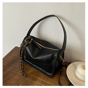 Détail du sac à main en cuir noir avec ferrures dorées et pendentif sur table en bois