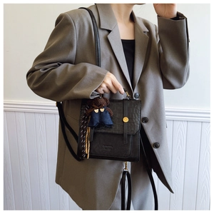 Detail of black faux crocodile leather crossbody bag with teddy bear charm on a grey blazer