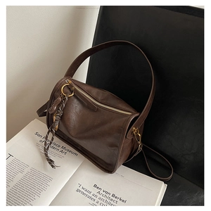 Détail d'un sac rétro marron foncé avec fermeture éclair dorée et pendentif tressé