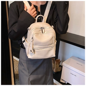 Close-up of cream faux leather backpack with multiple zipper pockets on a female model