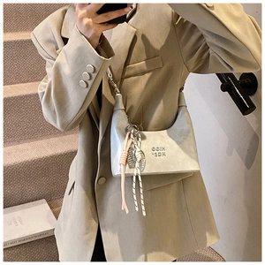 Détail du sac hobo gris avec logo embossé et pendentifs en corde décoratifs sur un costume