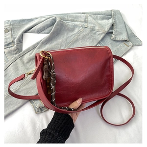 Détail du sac bandoulière en cuir bordeaux avec zip doré et pendentif nœud bicolore