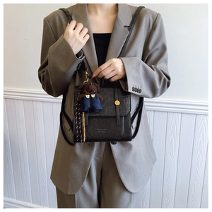 Detail of black faux crocodile leather backpack with metal buckle and plush bear charm