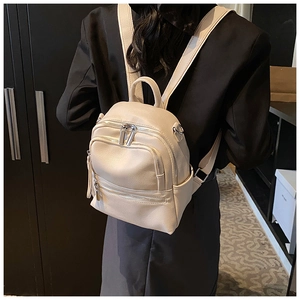 Detail of a beige mini faux leather backpack with multiple zippers and lychee texture
