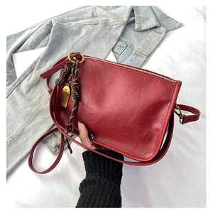 Détail d'un sac carré bordeaux avec pendentif cacahuète et cordon tressé sur du denim
