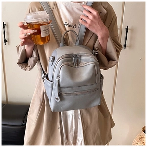 Detail of light grey pebbled leather backpack with dual zippers and side pockets on model