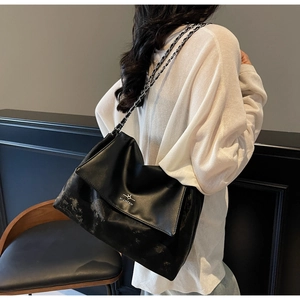 Detail of a large black leather tote bag with a chain strap shown on a shoulder
