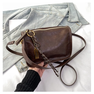 Détail d'un sac carré vintage marron foncé avec pendentif stylé et bandoulière longue