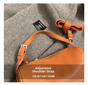Gros plan sur la bandoulière en cuir réglable et la boucle argentée du sac orange