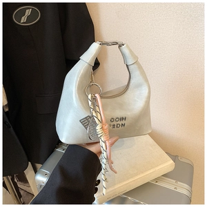 Détail du sac hobo en cuir bleu clair avec logo métallique et pendentif tressé