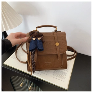 Detail of a brown crocodile-patterned backpack featuring a plush bear charm and metal rings