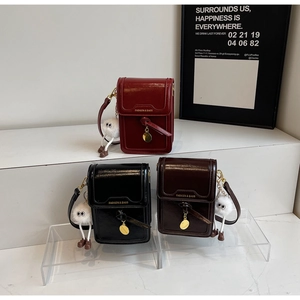 Detailed view of gloss mini crossbody bags in burgundy, black and brown with plush charms