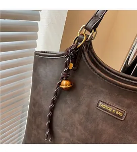 Dettaglio della borsa tote marrone scuro con trama vintage e ciondolo a campana dorata