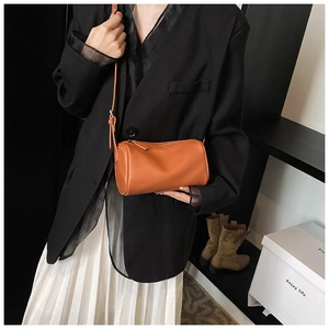Détail d'un sac bandoulière cylindrique marron montrant la texture du cuir et la sangle
